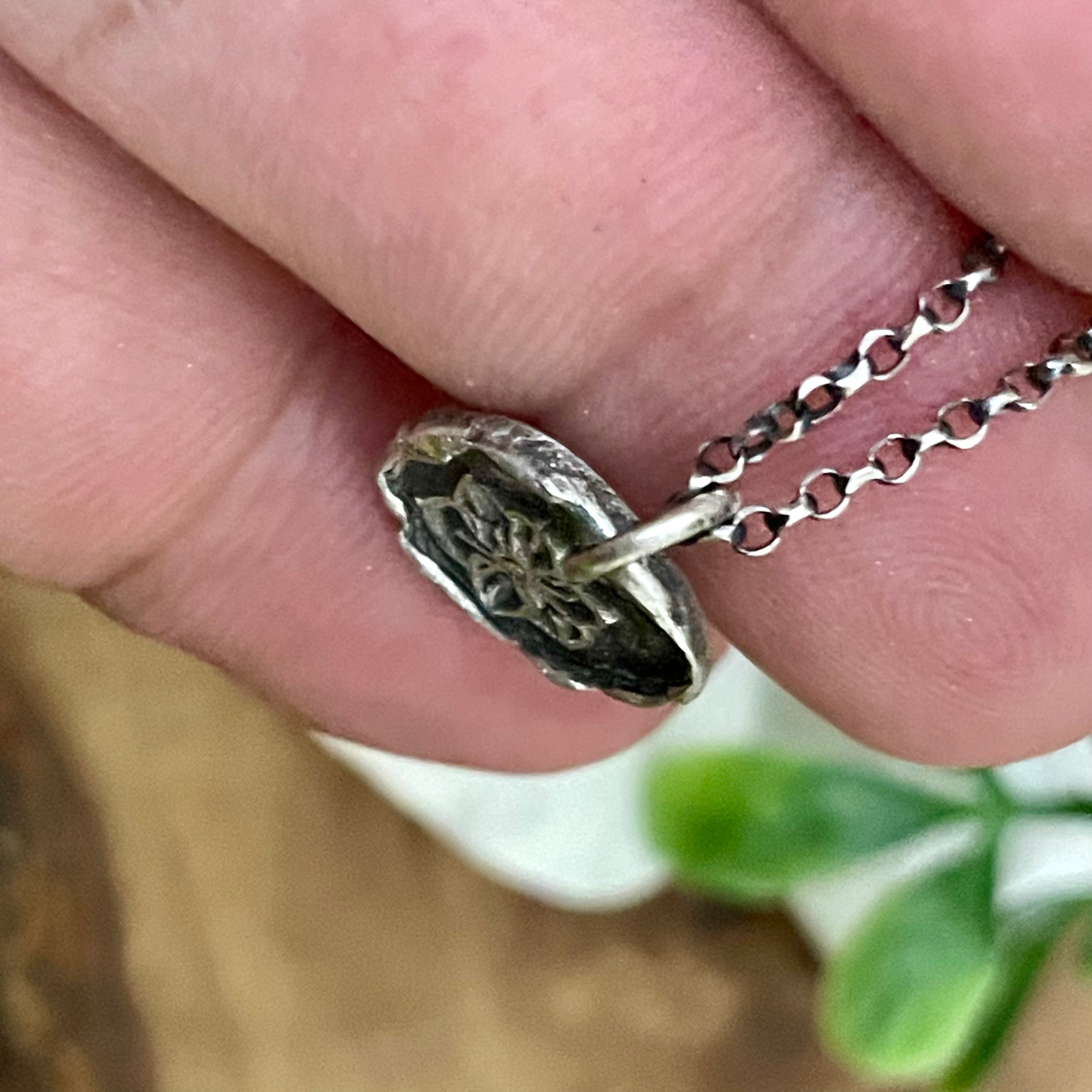 Close-up of a hand holding a silver pendant with a chain.