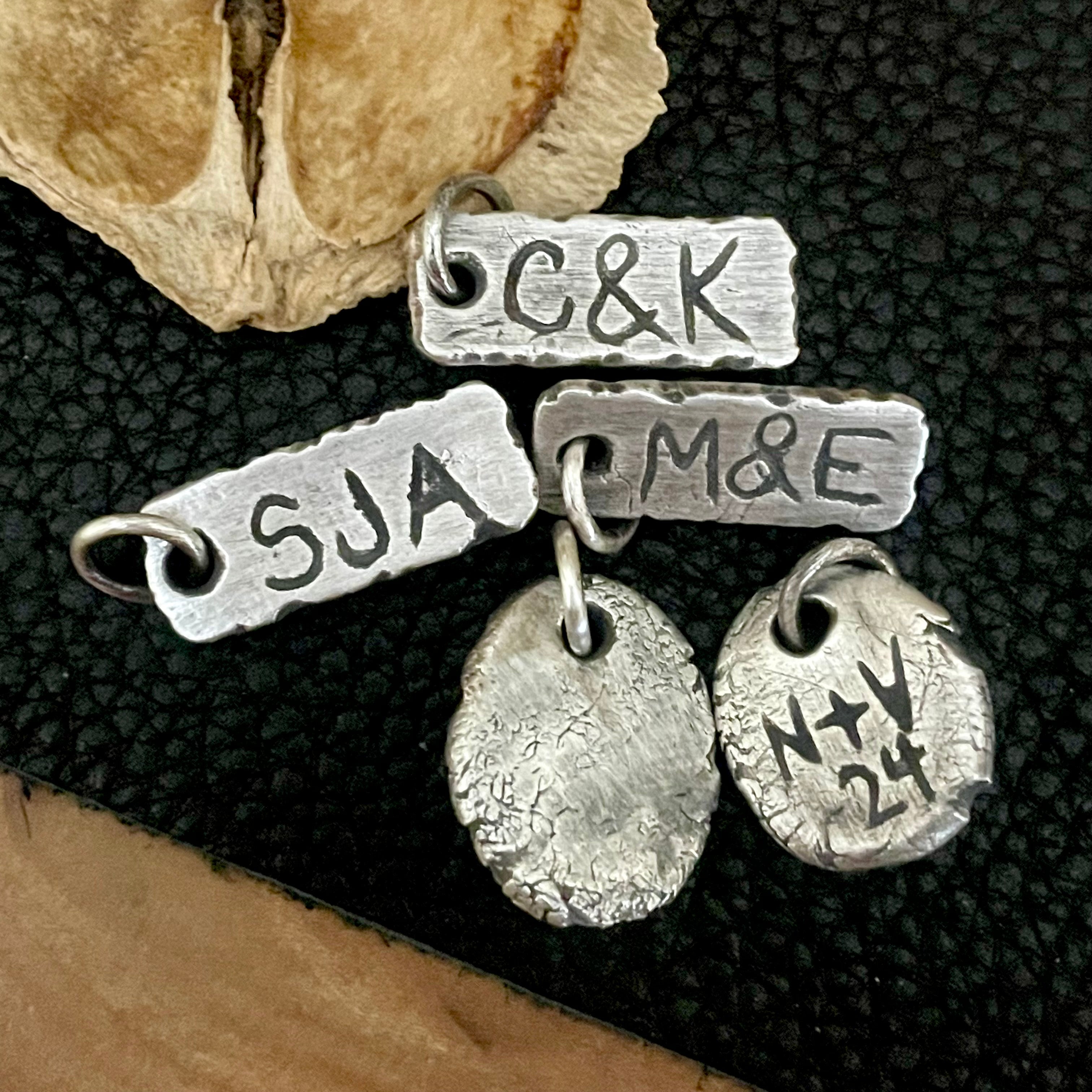 Rustic Sterling Silver personalized pendants on a textured black surface with wooden elements.