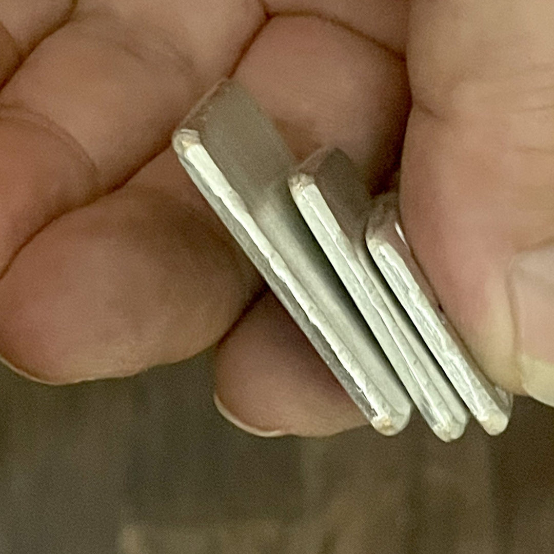 Side view of three solid sterling silver pendants in hand. 