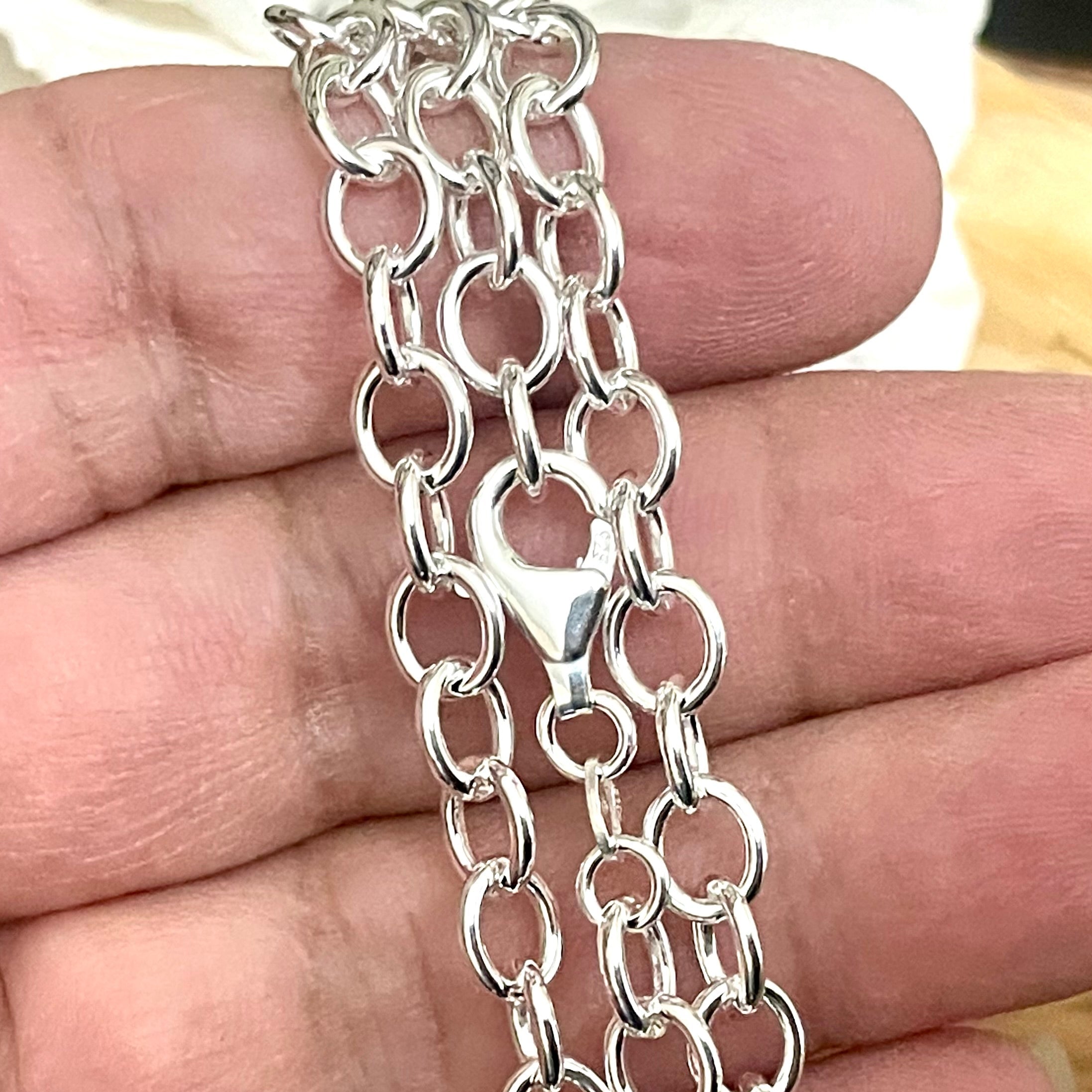 Womens wide oval chunky sterling Silver link chain held between fingers on a wooden surface