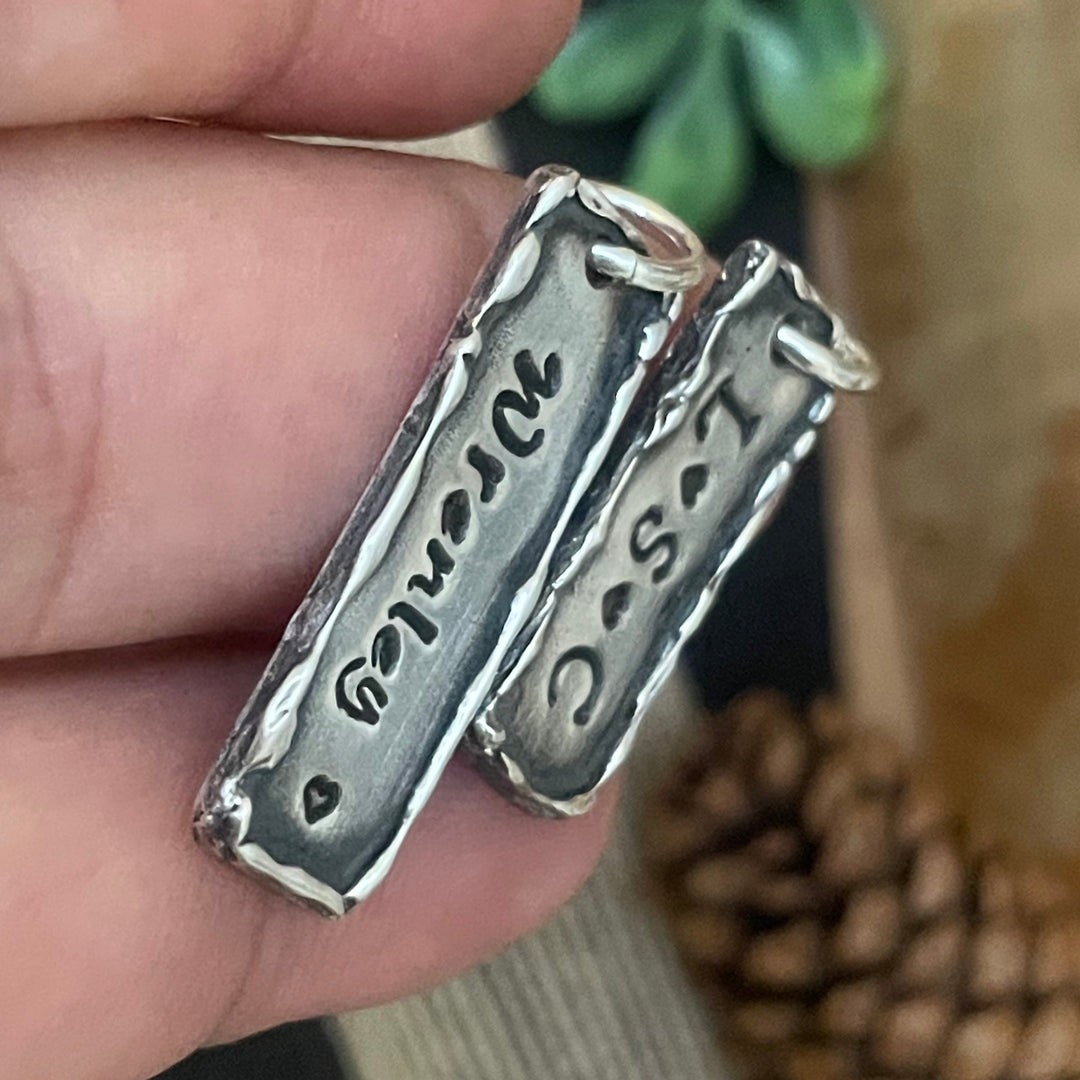Silver charm with engraved text held in a hand against a blurred natural background
