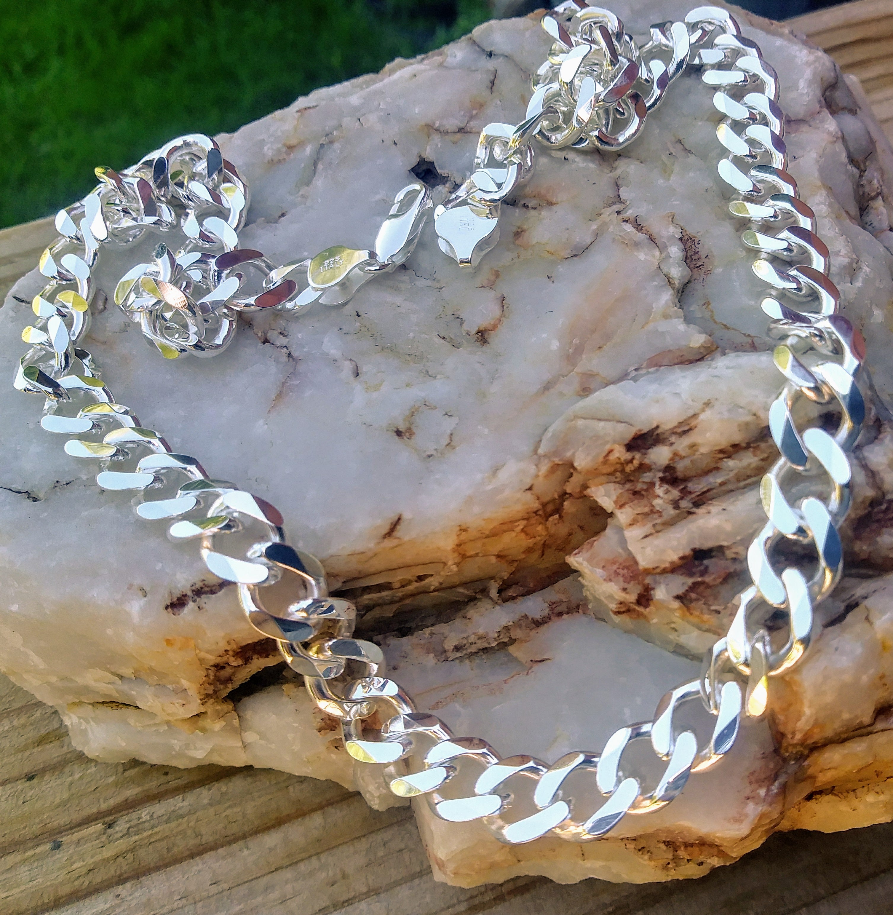 Heavy polished sterling silver curb chain necklace 10mm in width with lobster clasp, displayed on stone and wood. 
