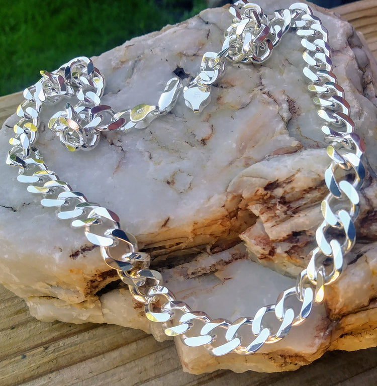 Heavy polished sterling silver curb chain necklace 10mm in width with lobster clasp, displayed on stone and wood. 