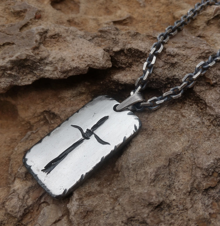 Rustic Silver Cross Necklace with hand carved barbwire design on solid sterling silver rectangle tag pendant. Hanging from 4mm anchor chain, oxidized. Displayed on stone.