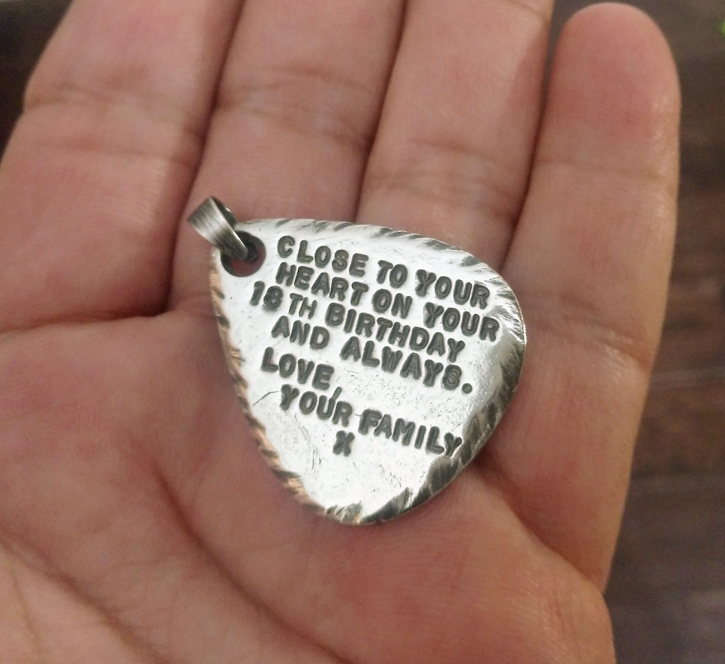 Custom birthday message engraved on textured sterling silver guitar pick pendant with rough edges, displayed in hand with bail. 