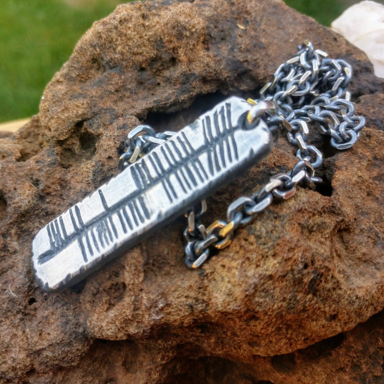 Custom silver Ogham Irish writing carved as name or word on pendant shown with sterling silver matching cable chain. Displayed on stone.