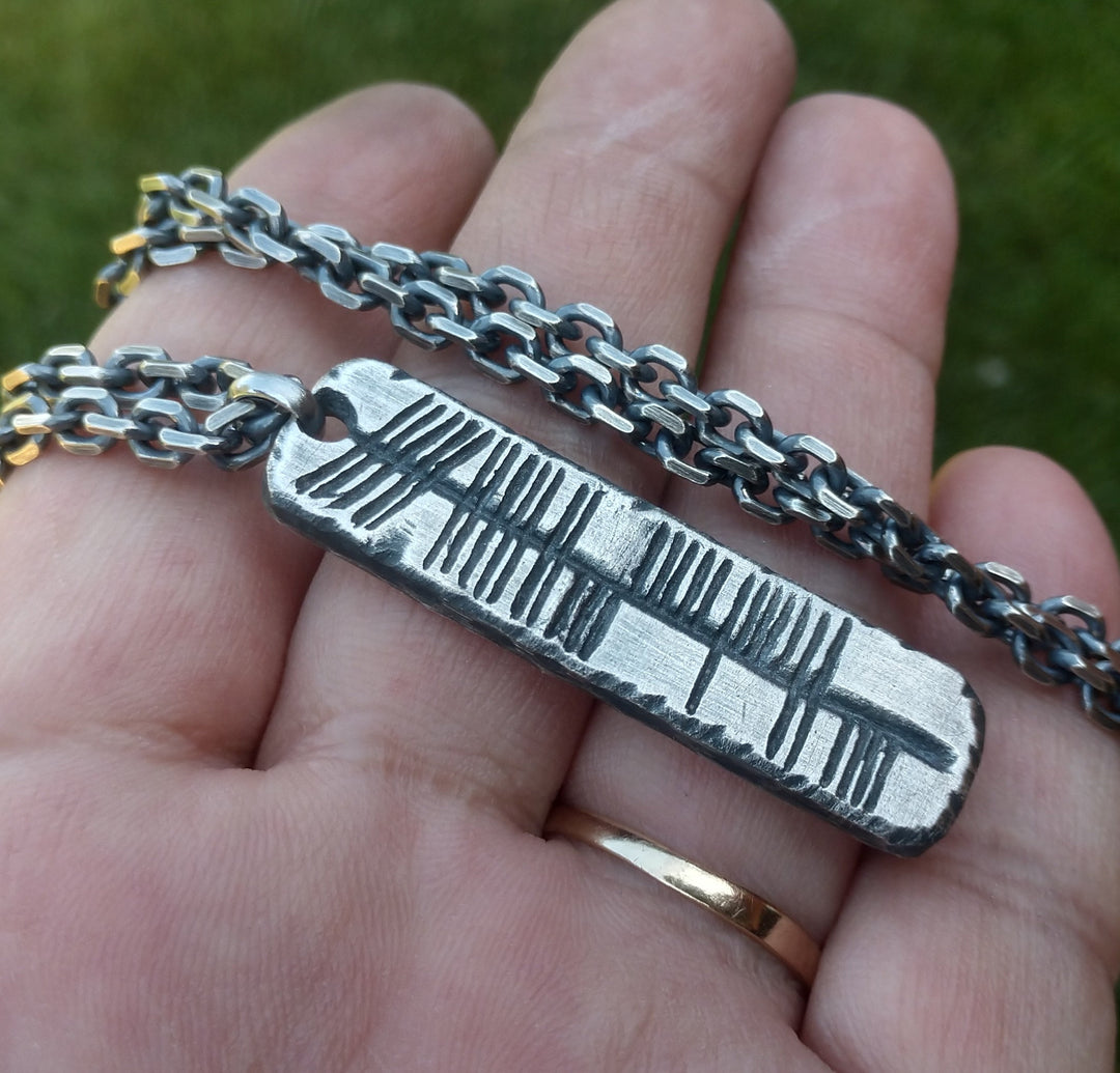 Custom engraved sterling silver rectangle bar pendant with ogham letters hanging from 4x5mm cable chain shown in hand. 