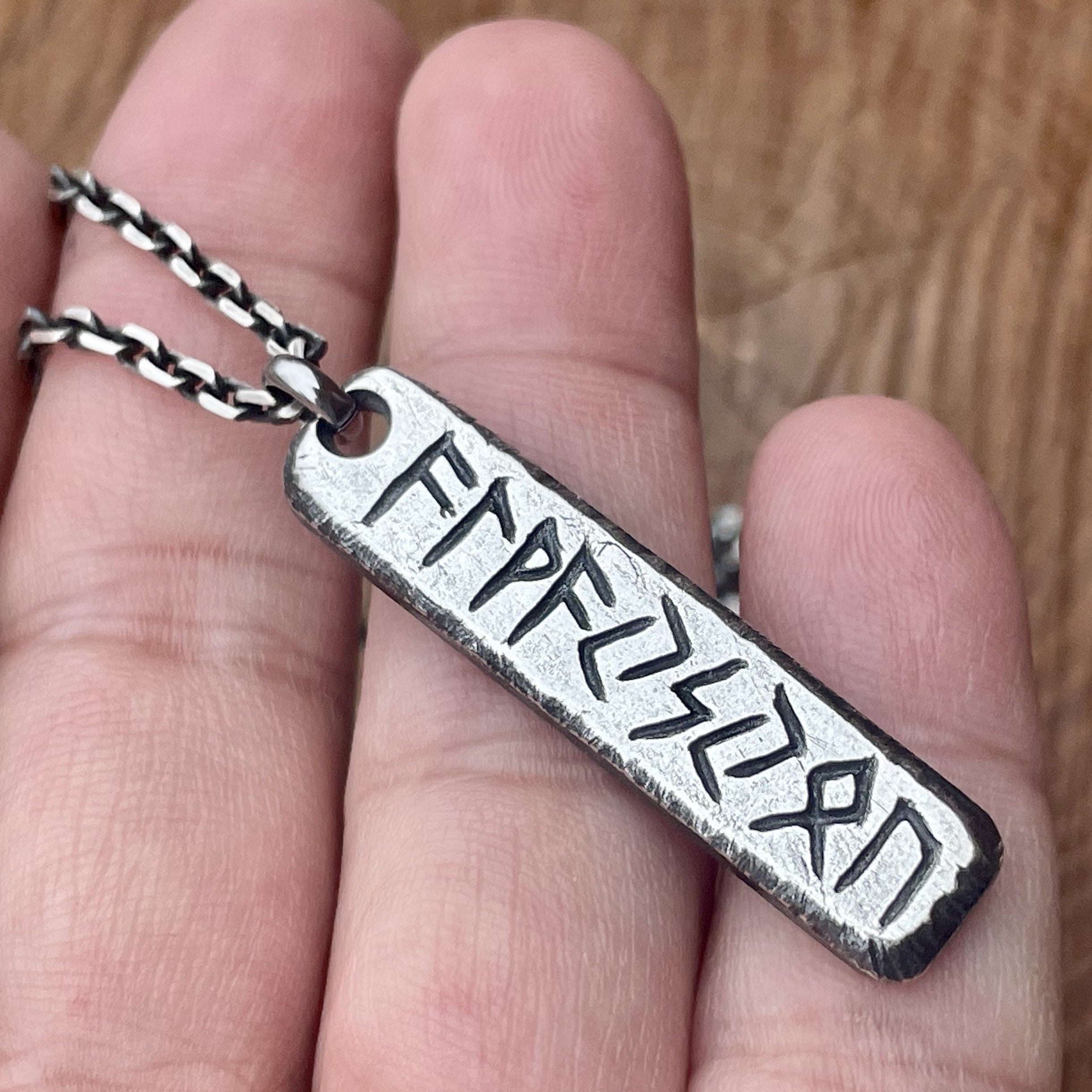Hand forged solid sterling silver elder futhark rune name or word pendant shown on oxidized sterling silver chain. Displayed on hand.