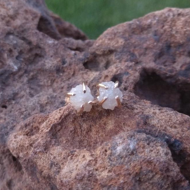 A pair of natural diamond earrings in gold claw setting displayed on rock