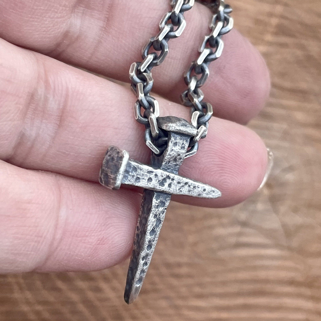 925 sterling silver nail cross pendant hanging from oxidized cable chain being held in hand.