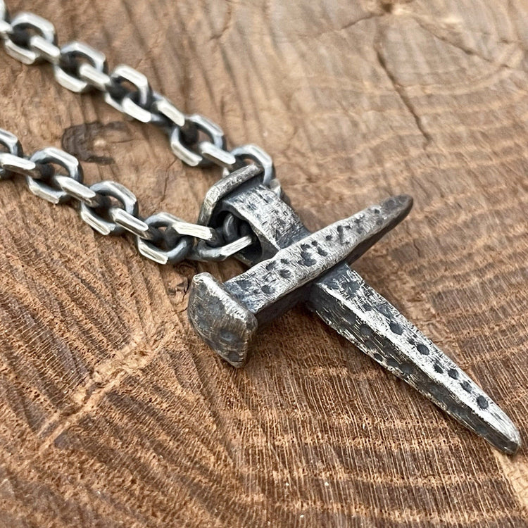 1.25 inch nail cross pendant and 4mm cable chain in oxidized sterling silver, displayed on wood.