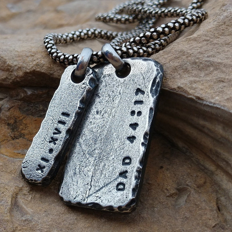 Oxidized thick sterling silver bar tag and rectangle pendant hanging from silver chain. Distressed hand carved edges with hand struck custom text. These pendants have roman numerals XI.XVII and Dad with bible verse numbers 44:17