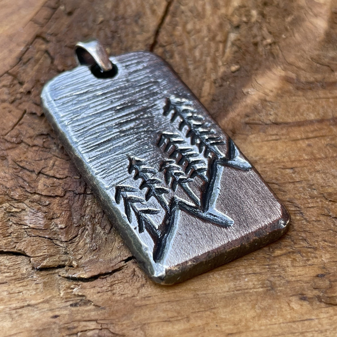 Oxidized sterling silver hand carved rectangle pendant with mountain and tree scene. Back side can be personalized. Displayed on wood background. 