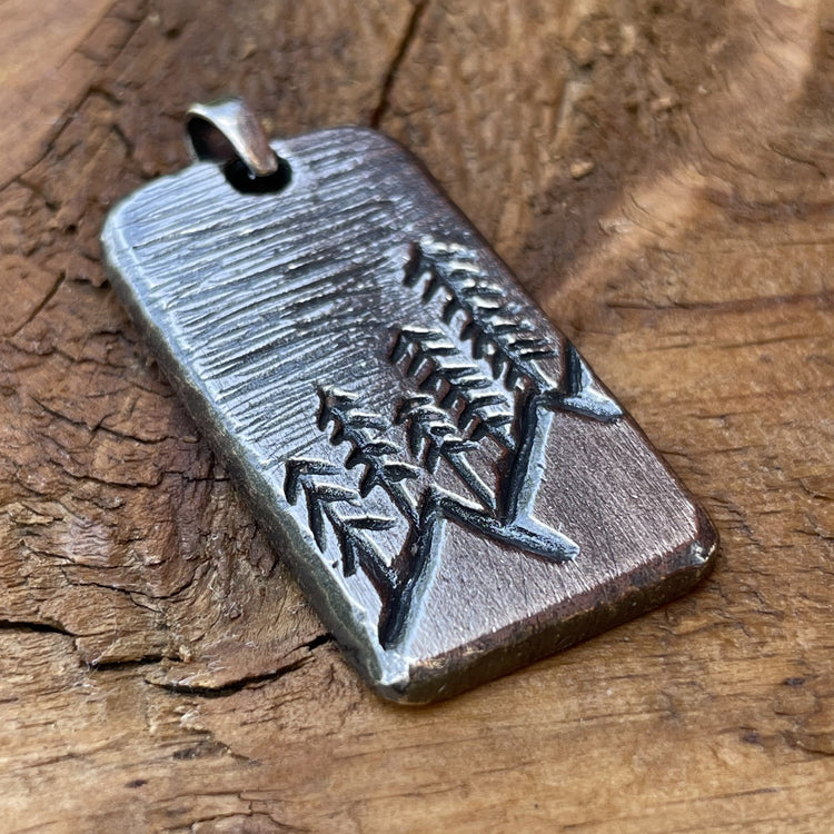 Oxidized sterling silver hand carved rectangle pendant with mountain and tree scene. Back side can be personalized. Displayed on wood background. 